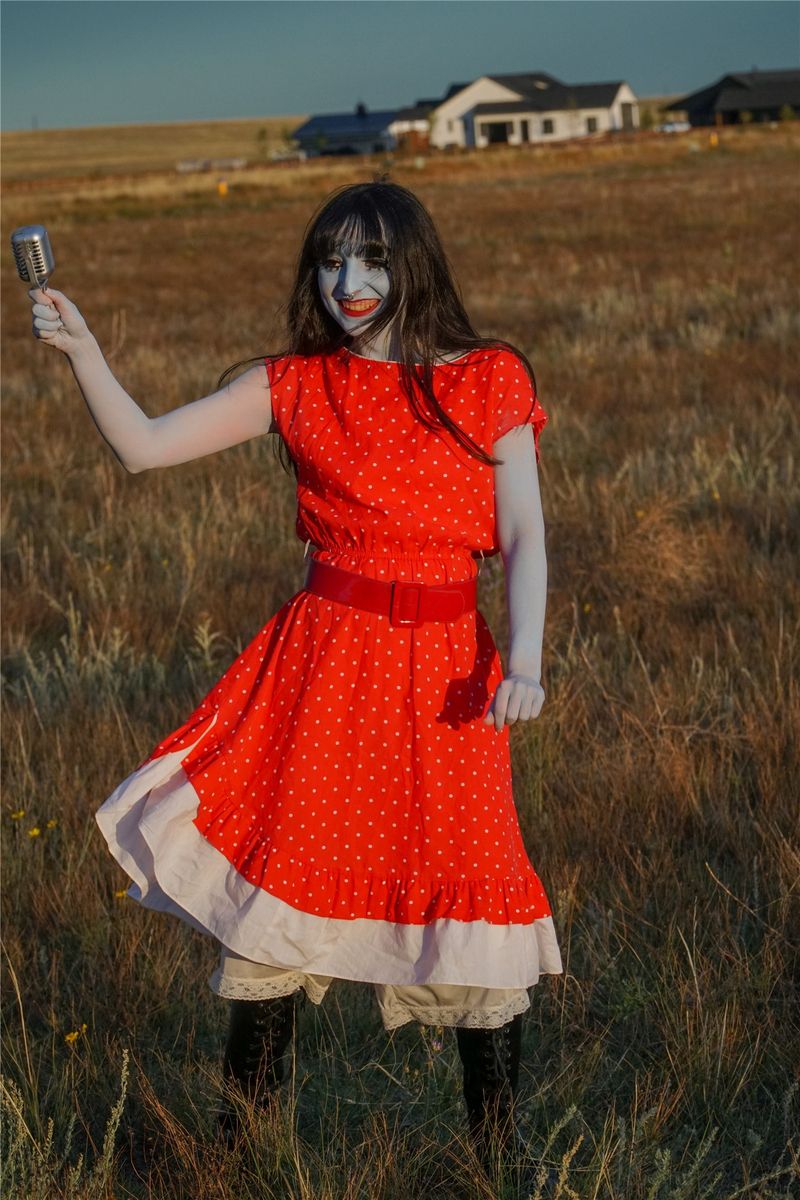 Hannah as Blue in a red dress, standing in a field